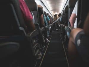 Imagem do corredor de um avião, dos dois lados várias pessoas sentadas nas poltronas