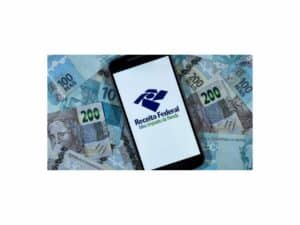 Imagem de uma foto de um celular com o logotipo da Receita Federal, entre cédulas de 200 e 100 reais. Foto utilizada para ilustrar uma notícia sobre a declaração do Imposto de Renda 2023.