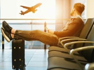 Imagem de uma pessoa sentada em uma cadeira de um aeroporto, com um avião ao fundo. Foto utilizada para ilustrar uma notícia sobre o programa Voa Brasil. Crédito: Unsplash.