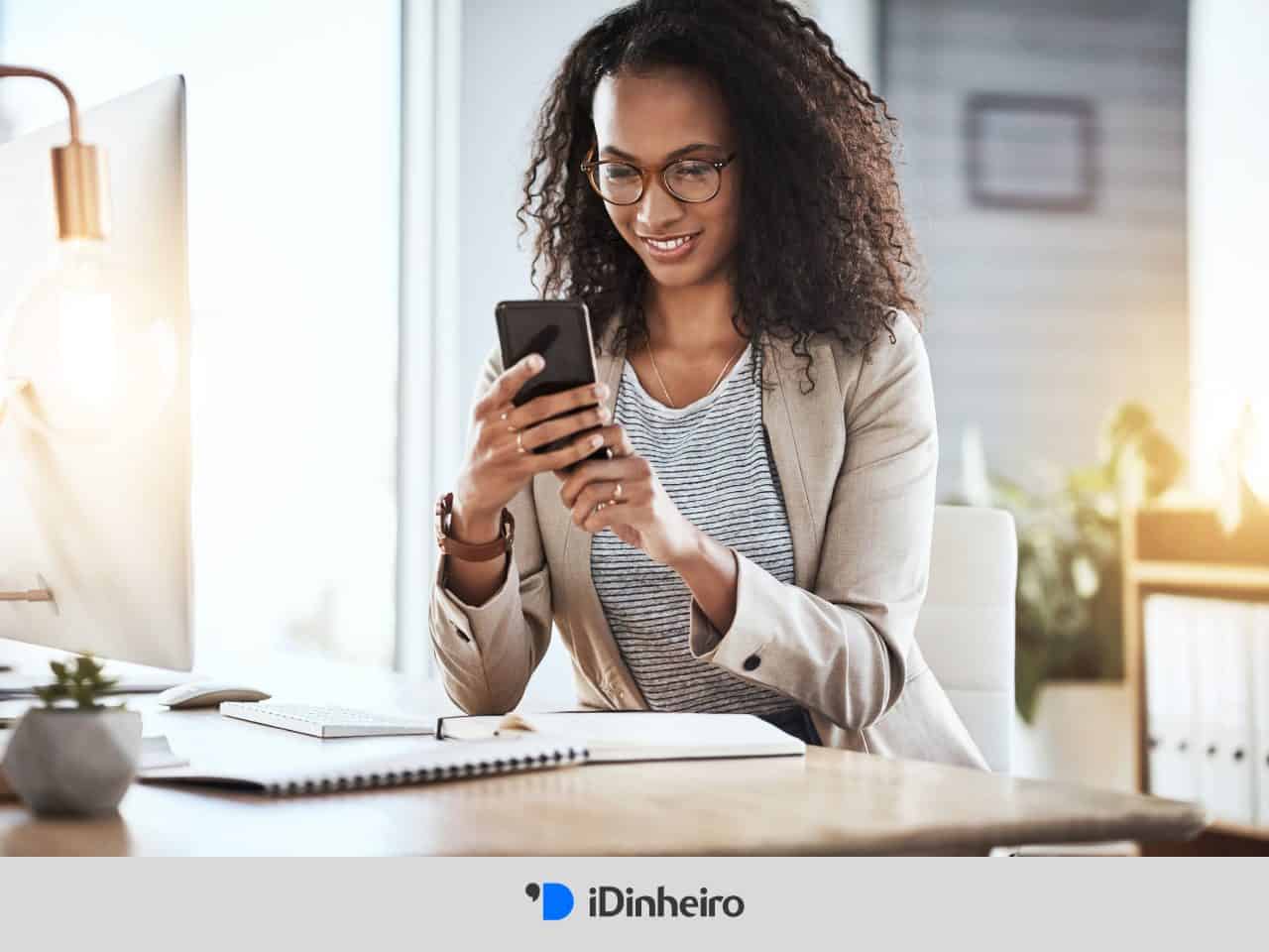 mulher sentada à mesa utiliza o celular para calcular o salário líquido